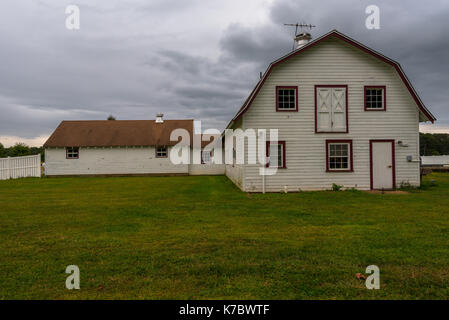 Un white barn su erba verde con un olandese syle tetto sotto cieli minacciosi. Foto Stock