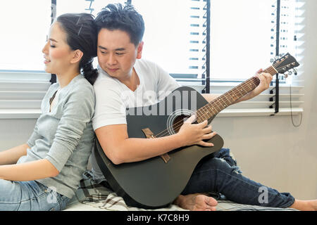 Coppie giovani suonare la chitarra tohether nella camera da letto di casa contemporanea per lo stile di vita moderno concetto Foto Stock