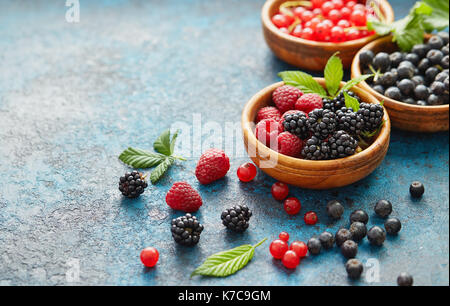 Varie frutta estiva in ciotole di legno. assortiti bacche fresche con foglie su sfondo di metallo. Foto Stock