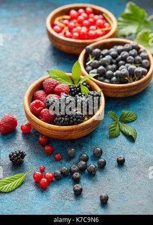 Varie frutta estiva in ciotole di legno. assortiti bacche fresche con foglie su sfondo di metallo. Foto Stock