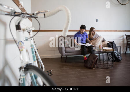 Paio di lettura di riviste mentre è seduto sul divano nella caffetteria Foto Stock