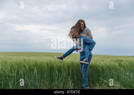 Giovane donna piggybacking sul campo erboso contro il cielo nuvoloso Foto Stock