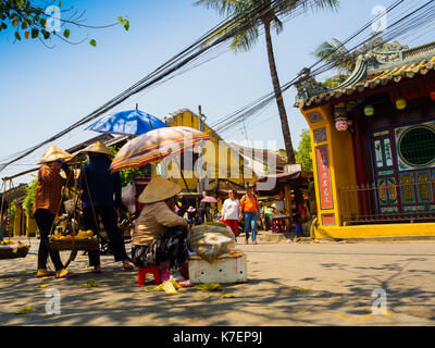 Hoian, vietnam, settembre 04 2017: donna non identificato a piedi e alcune donne con ombrello in mano e hangins nei loro spalle il cibo, nei pressi del tempio di hoian in Vietnam Foto Stock