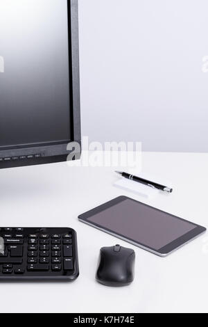 Tablet recante sul desktop vicino al monitor del PC e la tastiera in ambiente di lavoro. Foto Stock