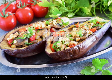 Melanzane ripiene con funghi, cipolle, carote, pomodori e i dadi su una piastra di metallo su sfondo grigio. cibo vegetariano. Il mangiare sano concetto. Foto Stock