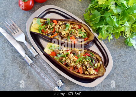 Melanzane ripiene con funghi, cipolle, carote, pomodori e i dadi su una piastra di metallo su sfondo grigio. cibo vegetariano. Il mangiare sano concetto. Foto Stock