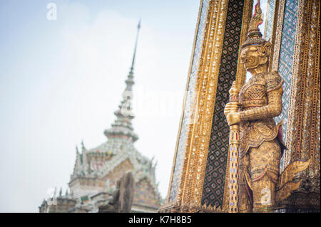 Statua Golden Demon Guardian fuori Phra Mondop (la biblioteca) con Phra Wiharn Yod in lontananza. Wat Phra Kaew. Il Grand Palace, Thailandia Foto Stock