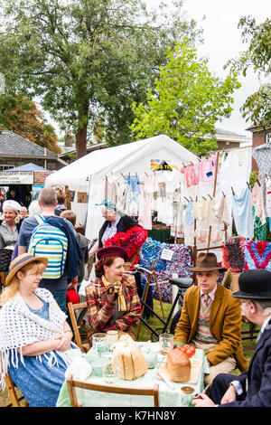 Due coppie mature vestita di classe superiore abbigliamento circa quaranta rivivere una guerra mondiale due picnic a una tabella con un lavaggio appeso dietro di loro. Saluto alla 40's weekend a Chatham Historic Dockyard. Uomo anziano fumare una tubazione. Foto Stock