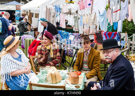 Due coppie mature vestita di classe superiore abbigliamento circa quaranta rivivere una guerra mondiale due picnic a una tabella con un lavaggio appeso dietro di loro. Saluto alla 40's weekend a Chatham Historic Dockyard. Uomo anziano fumare una tubazione. Foto Stock