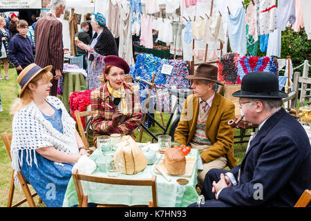 Due coppie mature vestita di classe superiore abbigliamento circa quaranta rivivere una guerra mondiale due picnic a una tabella con un lavaggio appeso dietro di loro. Saluto alla 40's weekend a Chatham Historic Dockyard. Uomo anziano fumare una tubazione. Foto Stock