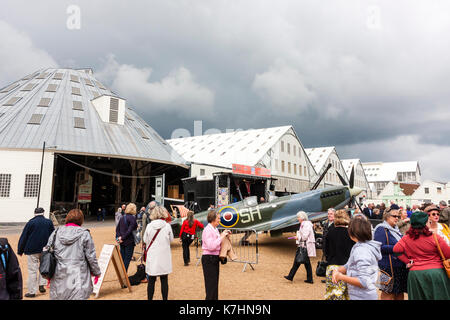 Inghilterra, Chatham dockyard. Evento, Saluto alla 1940s. Le persone in attesa in linea per ottenere le loro foto scattata nel pozzetto di una guerra mondiale due Spitfire aereo da combattimento. Molto scure nuvole temporalesche overhead. Foto Stock