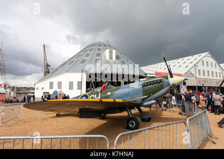 Inghilterra, Chatham dockyard. Evento, Saluto alla 1940s. Le persone in attesa in linea per ottenere le loro foto scattata nel pozzetto di una guerra mondiale due Spitfire aereo da combattimento. Molto scure nuvole temporalesche overhead. Foto Stock