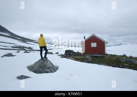 Uomo vicino tipici norvegesi red casa in legno vicino alla celebre aurlandsvegen (bjorgavegen) strada di montagna in Aurland, Norvegia in estate Foto Stock