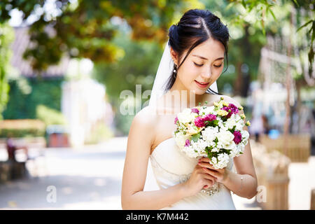Bella e felice di giovani asiatici sposa indossa velo nuziale tenendo un mazzo di fiori. Foto Stock