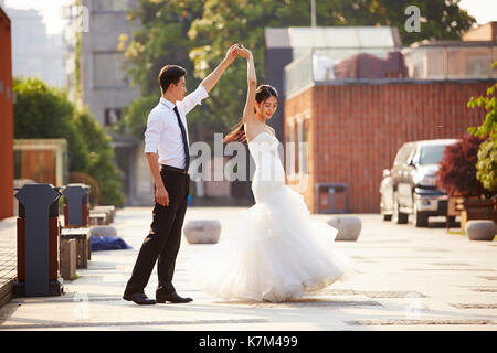 Giovani asiatici sposa e lo sposo in abito da sposa in ballo nel parcheggio. Foto Stock