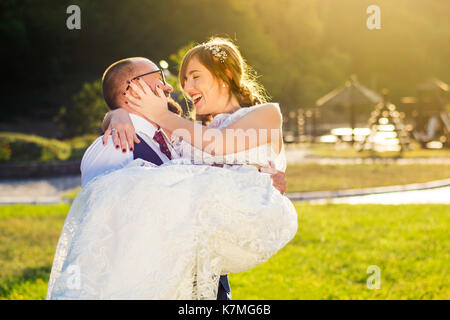 Lo sposo holding sposa nel suo stemma, sposi divertendosi Foto Stock