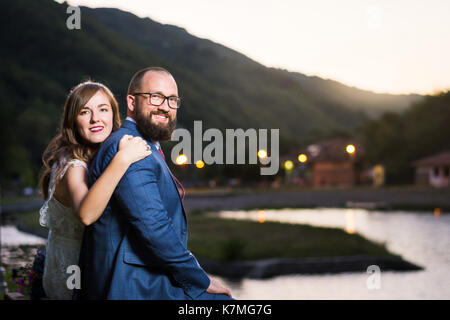 Sposa e lo sposo seduta dal lago alla sera Foto Stock