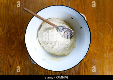 Azzimo pasta di lievito con il cucchiaio di legno in smalto bianco recipiente metallico sul tavolo di legno dal di sopra. Foto Stock