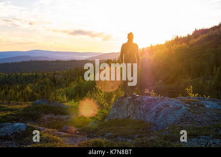 Giovane uomo in piedi su una grande pietra che guarda al tramonto in mezzo al paesaggio Foto Stock