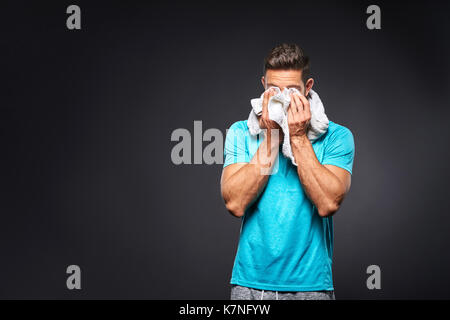 Un bel giovane atleta sensazione di stanchezza e strofinando il viso con un asciugamano Foto Stock