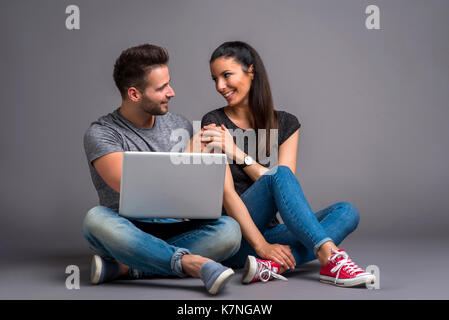 Una bella coppia giovane seduto per terra e che guardano un notebook e sorridente Foto Stock