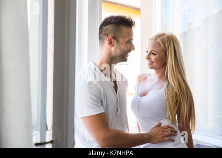 Una bella coppia giovane in piedi presso la finestra a casa. Foto Stock