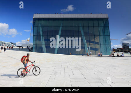 Un ciclista tiene in vista della piazza lastricata e vetro esterno del Teatro dell'Opera di Oslo, Norvegia Foto Stock