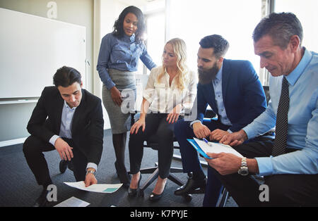 Diversi gruppi di lavoro concentrato professionisti discutendo di documenti sparsi sul pavimento mentre avente un incontro insieme in un luminoso ufficio moderno Foto Stock