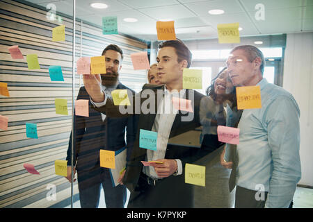 Un gruppo di persone di affari il brainstorming con note adesive sulla finestra in vetro Foto Stock