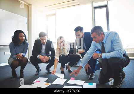 Il team di Business il brainstorming in ufficio, accovacciato a guardare un assortimento di idee sul pavimento Foto Stock