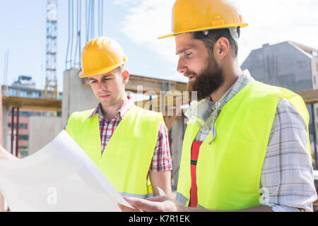 Due giovani lavoratori edili analizzando insieme il piano di un Foto Stock