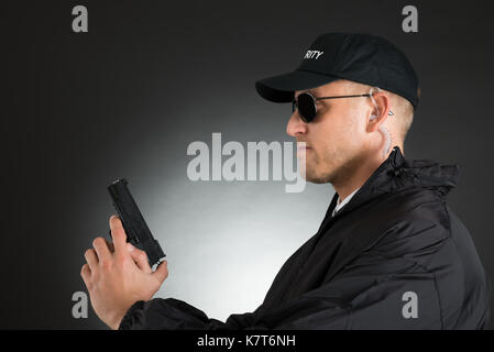 Ritratto di giovane bodyguard tenendo la pistola su sfondo nero Foto Stock