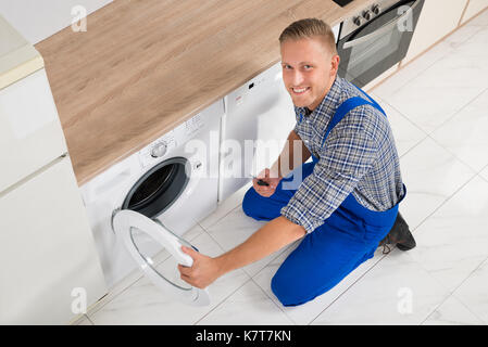 Felice tecnico maschio con un cacciavite la riparazione della macchina di lavaggio Foto Stock