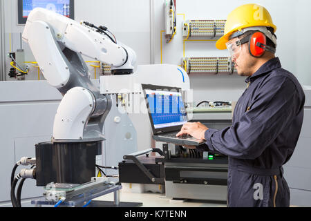 Ingegnere utilizzando computer portatili per la manutenzione automatica di mano robotica di macchina utensile in smart factory, industria 4.0 concetto Foto Stock