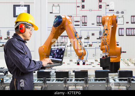 Ingegnere utilizzando computer portatili per la manutenzione automatica di mano robotica di macchina utensile in smart factory, industria 4.0 concetto Foto Stock