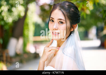 Outdoor ritratto della bella e felice di giovani asiatici sposa indossa velo nuziale. Foto Stock