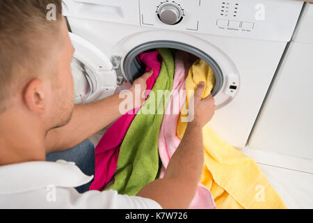 Close-up di giovane uomo carico asciugamani colorati nella macchina di lavaggio Foto Stock