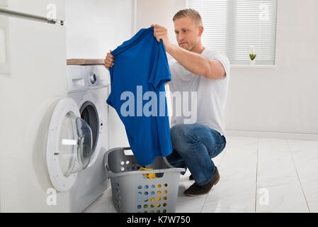 Giovane uomo guardando t-shirt mentre utilizzando la lavatrice apparecchio in cucina Foto Stock