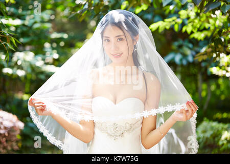 Outdoor ritratto della bella e felice di giovani asiatici sposa indossa velo nuziale. Foto Stock