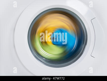 Close-up di lavatrice porta con vestiti variopinti rotante all'interno di Foto Stock