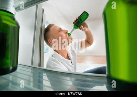 Giovane uomo a bere birra nella parte anteriore del frigorifero aperto con bottiglie di birra Foto Stock