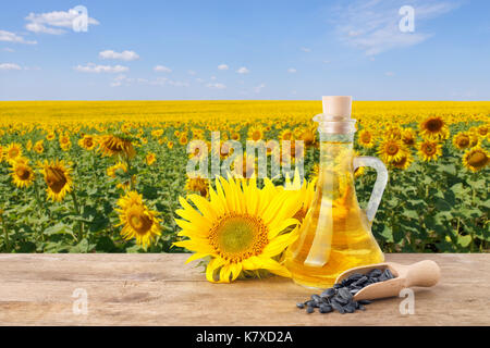 Olio di semi di girasole in una bottiglia di vetro, semi nel convogliatore, girasoli freschi sul tavolo di legno con sfondo naturale. blooming campo di girasoli con cielo blu. agric Foto Stock