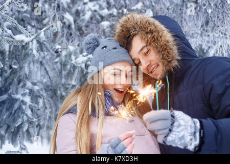 Coppia giovane con botti in inverno foresta. famiglia sorridente con luci di bengala. sorridenti giovane con holiday botti festeggiano il Natale di fuori Foto Stock