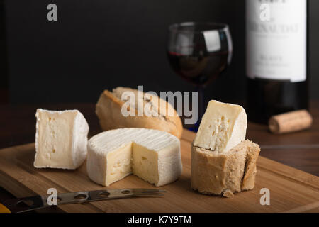 Varietà di formaggio su un asse di legno con vino e bottiglia Foto Stock