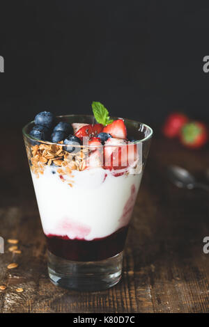 Yogurt con muesli, mirtilli e fragole in vetro su un tavolo di legno. closeup vista verticale. concetto di mangiare sano, dieta e mangiare pulito Foto Stock