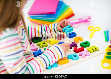 Bambino facendo i compiti per la scuola al bianco scrivania in legno per istruzione abc puzzle giocattoli per bambini. Felice torna a scuola studente. kid alfabeto di apprendimento lettere Foto Stock