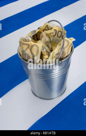 Bandiera greca con un secchio metallico di banconote da 200 euro. Per la crisi finanziaria greca e il salvataggio, la riduzione del debito greco, la crisi economica greca, la recessione greca. Foto Stock