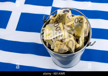 Bandiera greca con un secchio metallico di banconote da 200 euro. Per la crisi finanziaria greca e il salvataggio, la riduzione del debito greco, la crisi economica greca, la recessione greca. Foto Stock