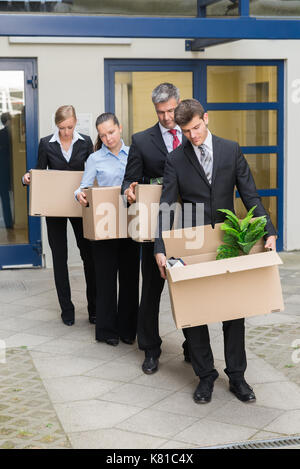 Deluso gli imprenditori in piedi in fila con scatole di cartone al di fuori dell'ufficio Foto Stock