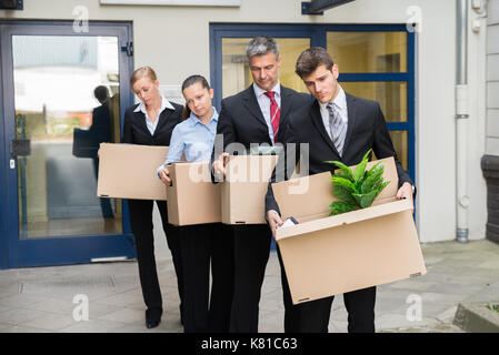 Deluso gli imprenditori in piedi in fila con scatole di cartone al di fuori dell'ufficio Foto Stock